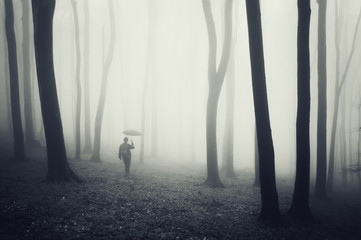 man with umbrella walking in a dark forest with fog