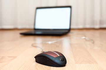 Opened laptop and computer mouse on the floor in the room