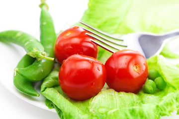tomato,peas and lettuce with a fork on a plate isolated on white