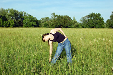 Young woman doing fitness exercises on green meadow