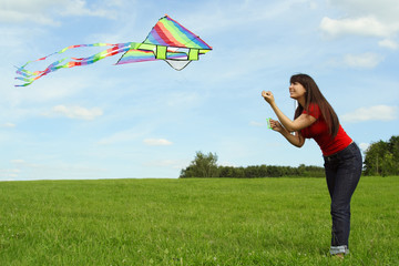Young girl in red shirt flying kite on summer meadow