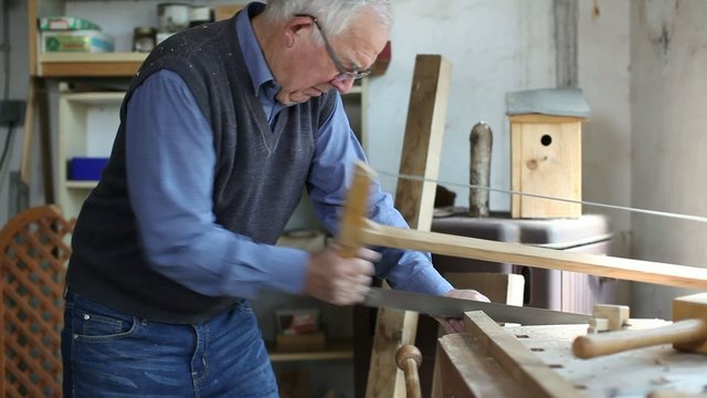 &auml;lterer mann s&auml;gt holzbalken in der werkstatt