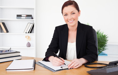 Beautiful red-haired female in suit writing on a notepad and pos