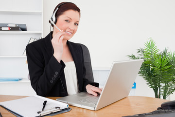 Young attractive red-haired female in suit typing on her laptop