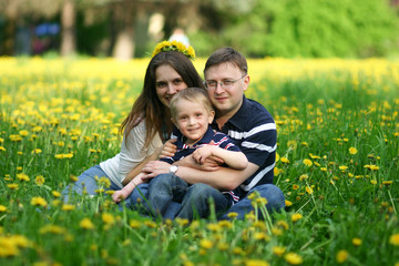 Naklejka na ściany i meble Happy young family of three on field of dandelions