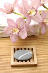 pink orchid on towel with wooden bowl of stone