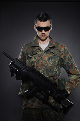 Young soldier in camouflage and ammunition with a rifle. studio