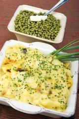 Cooked peas and scalloped potatoes in ceramic dishes