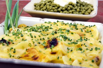 Cooked peas and scalloped potatoes in ceramic dishes