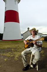 Guitarist playing acoustic instrument near lighthouse