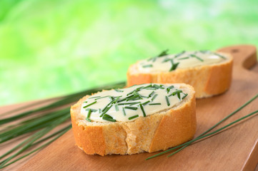 Baguette slices with soft cheese and chives on cutting board