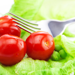 tomato,peas and lettuce with a fork on a plate isolated on white