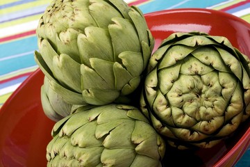 Obraz premium Raw artichokes on a red ceramic plate with colorful background