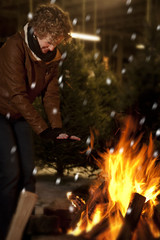 Woman warming hands by fire at christmas tree lot