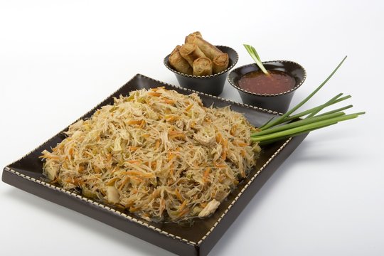 Pancit on a ceramic dish with egg rolls and sweet and sour sauce