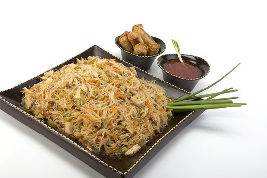 Pancit on a ceramic dish with egg rolls and sweet and sour sauce