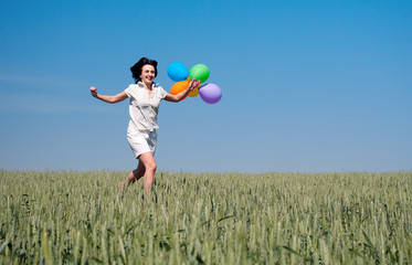 Woman running on the wheat field with colorful balloons