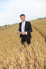 Businessman with electronic tablet standing in wheat field