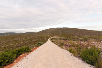 Emtpy gravel roads through mountains against cloudy sky