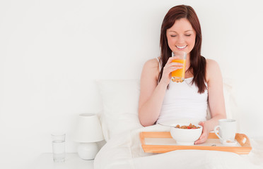 Obraz na płótnie Canvas Beautiful red-haired female drinking a glass of orange juice whi