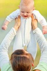 Mother holding laughing baby outdoors at summer day.