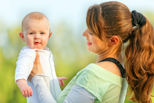 Smiling young mother holding surprised baby in hands