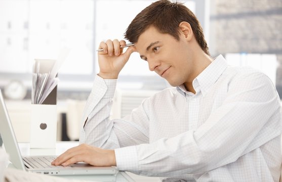Young office worker thinking in office with laptop