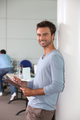 Fototapeta premium Man in office leaning against wall holding clipboard and pen