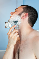 Young man shaving his beard in the bathroom