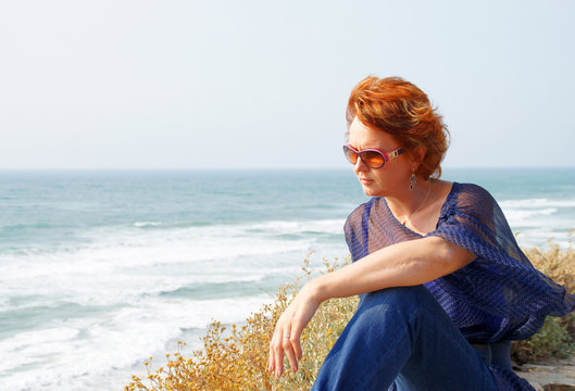 Beautiful middle-aged woman sits by the sea