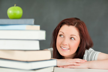 Young student looking at the apple on the top of her books