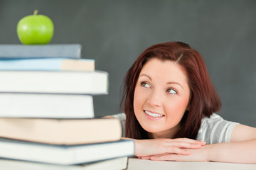 Young student looking at the apple on the top of her books