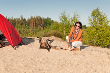 Camping happy woman sitting by campfire on beach