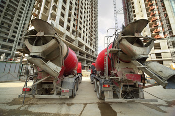 Two concrete mixer stand near unfinished tall high-rise building