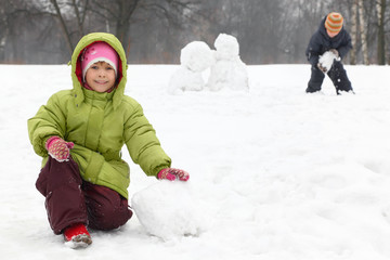 Fototapeta na wymiar Two children play on outdoor in winter and sculpt snowman