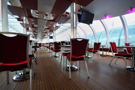 Light restaurant on board of ship, rows of tables and red chairs