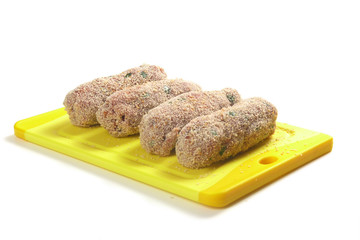 rohe, panierte Fleischrollen  auf gelbem Brett / raw, fried meat