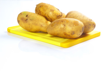 frische Kartoffeln auf gelbem Schneidbrett vor weißem Hintergrun