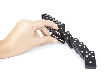 a hand breaking dominos fall by stop one in the middle.