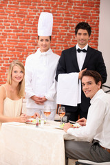 A couple being served by a waiter and a chef in a restaurant