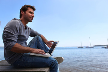 Man sat with computer by lake