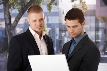 Two businessmen with laptop outside of office