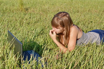 Девочка лежит в поле с ноутбуком