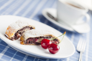 Poppy seed strudel with cherry and cup of coffee or tea.