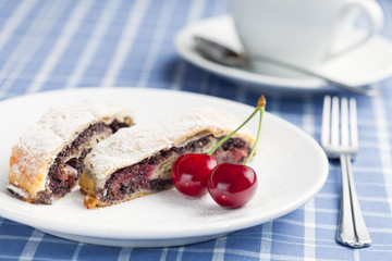 Poppy seed strudel with cherry and cup of coffee or tea.