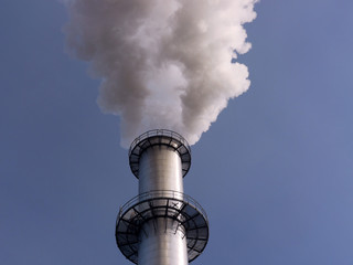 Ein rauchender Industrieschornstein vor strahlend blauem Himmel.