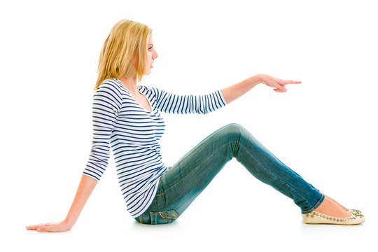 Beautiful teengirl sitting on floor and pointing at copy-space