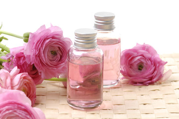 bottles with essential oil and pink dahlia flower on woven mat