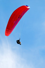 Red paraglider flying in blue sky