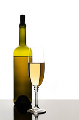 Bottle and glass of white wine against dark